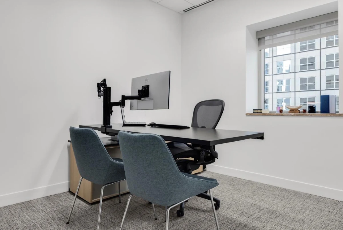 Executive office setup with an ergonomic height-adjustable black desk, mesh office chair, and two fabric visitor chairs